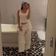 Woman takes a mirror selfie in white cargo pants, white tank top and a head scarf. 